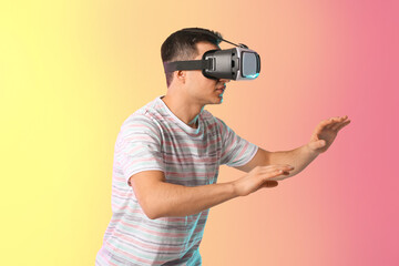 Wall Mural - Young man with virtual reality glasses on color background