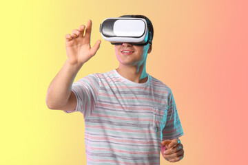 Wall Mural - Young man with virtual reality glasses on color background