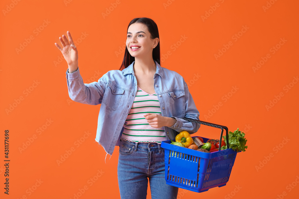 Young woman with shopping basket on color background
