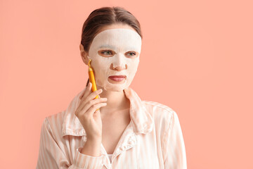 Wall Mural - Beautiful young woman with sheet facial mask and massage tool on color background