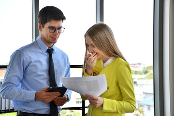 A business man in a blue shirt and a business woman in a yellow shirt were having fun discussing the work the two were doing together.