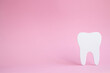 White figurine of a human tooth on a pink background with place for text