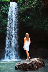 Wall Mural - Young woman travel in Bali rainforest. Happy girl enjoy jungle nature. Stand in natural pool under waterfall, see on falling water. Walking day tour, hiking activity adventure on family summer holiday