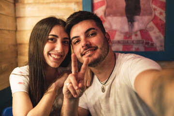 Poster - Cheerful young couple taking a selfie; the guy is showing a V-sign