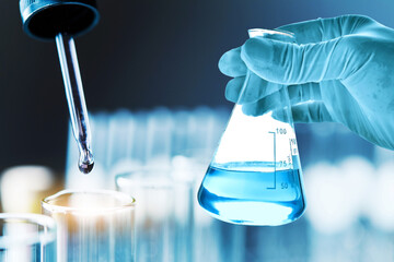 Wall Mural - hand of scientist holding flask with lab glassware in chemical laboratory background, science labora