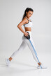 © nikolas_jkd - Fitness woman working out with resistance band on gray background. Athletic girl exercises with expander