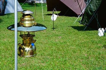 Wall Mural - Close up image of vintage hanging brass camping lantern with field tents group on green lawn in camping area at natural parkland