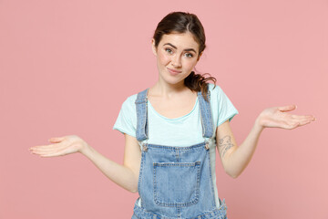 Wall Mural - Young confused mistaken uncertain doubtful expresive caucasian woman in denim clothes blue tshirt spread hands oops gesture isolated on pastel pink background studio portrait People lifestyle concept