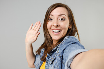 Poster - Close up young fun cheerful smiling happy caucasian woman 20s wear casual denim jacket yellow t-shirt doing selfie shot on mobile phone waving hand greeting isolated on grey color background studio