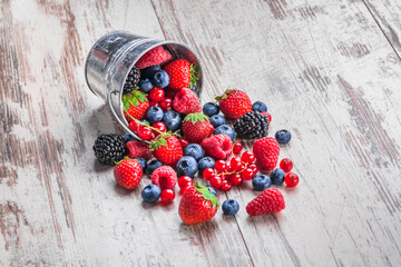 Wall Mural - Berries fresh assorted spilled ready to eat kitchen vibrant color arrangement in rustic tin can on old white wooden table studio shot