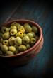 Green fresh olives in brown crockery jar on blue background vibrant color slanted arrangement front view low light studio shot