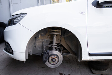 Car without a wheel in auto repair shopRemoved front wheel, close up view photo. Car without wheel and lift up by hydraulic, waiting for tire replacement.