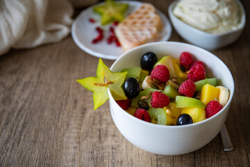 White bowl of fresh healthy fruit salad on wooden background with carambola star