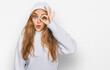 Young caucasian girl wearing wool sweater and winter cap doing ok gesture shocked with surprised face, eye looking through fingers. unbelieving expression.