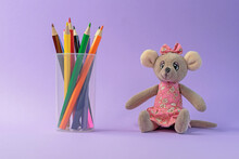 Colored Pencils In A Plastic Cup And A Toy Mouse On A Lilac Background.