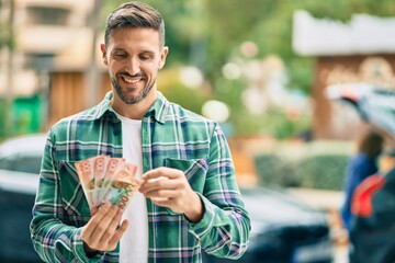 Wall Mural - Young caucasian man smiling happy standing counting new zealand dollars banknotes at the city.