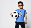 studio portrait of preschool little asian boy in trendy trendy sunglasses blue t-shirt print soccer player holding soccer ball looking at camera.