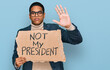 © Krakenimages.com - Young handsome hispanic man holding not my president protest banner with open hand doing stop sign with serious and confident expression, defense gesture