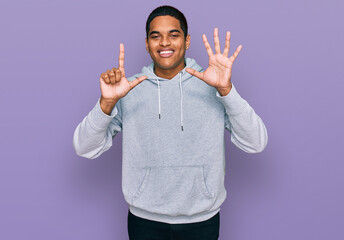 Young handsome hispanic man wearing casual sweatshirt showing and pointing up with fingers number seven while smiling confident and happy.