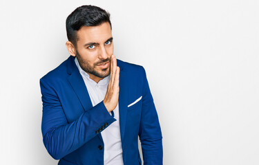 young hispanic man wearing business jacket hand on mouth telling secret rumor, whispering malicious 