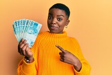 Young African American Woman Holding 100 Brazilian Real Banknotes Smiling Happy Pointing With Hand And Finger