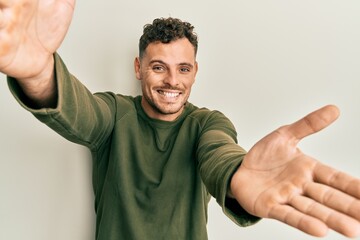 Sticker - Young hispanic man wearing casual clothes looking at the camera smiling with open arms for hug. cheerful expression embracing happiness.