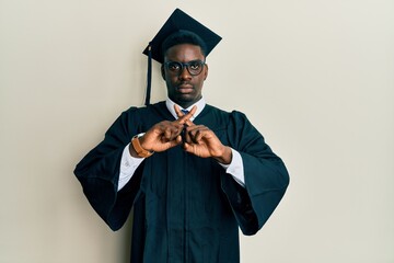 Wall Mural - Handsome black man wearing graduation cap and ceremony robe rejection expression crossing fingers doing negative sign