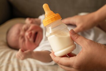 Mother trying to feed her hungry fussy baby with a bottle of milk.