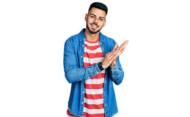 Young hispanic man with beard wearing casual denim jacket clapping and applauding happy and joyful, smiling proud hands together