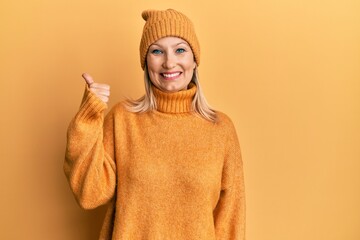 Middle age caucasian woman wearing wool winter sweater and hat smiling happy and positive, thumb up doing excellent and approval sign