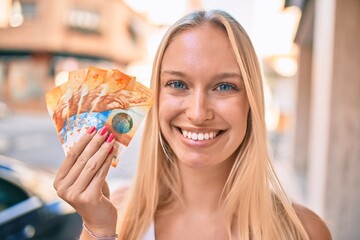 Sticker - Young blonde girl smiling happy holding swiss franc banknotes walking at the city.