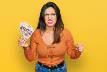 Sticker - Beautiful hispanic woman holding mexican pesos annoyed and frustrated shouting with anger, yelling crazy with anger and hand raised