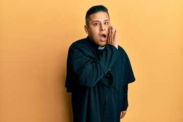 Canvas Print - Young latin priest man standing over yellow background hand on mouth telling secret rumor, whispering malicious talk conversation