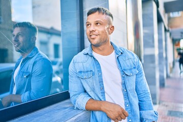 Wall Mural - Young caucasian man smiling happy leaning on the wall at the city.