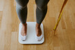 © shevtsovy - Woman step on Weighing Scale for Measuring Body Weight At Home. . Close up of a woman legs measuring weight with scale at home and holding measuring tape. Weight management.