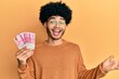 © Krakenimages.com - Young african american man with afro hair holding 100000 indonesian rupiah celebrating achievement with happy smile and winner expression with raised hand