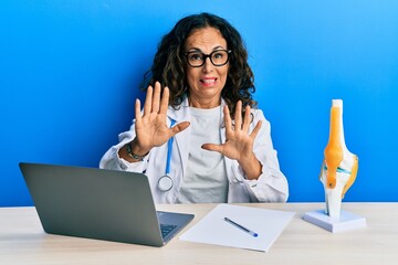 Poster - Beautiful middle age woman doctor at orthopedic clinic afraid and terrified with fear expression stop gesture with hands, shouting in shock. panic concept.