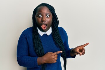 Wall Mural - Young black woman with braids pointing up with fingers to the side afraid and shocked with surprise and amazed expression, fear and excited face.