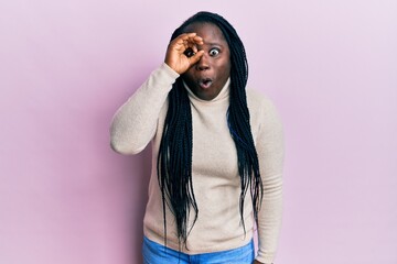 Poster - Young black woman with braids wearing casual winter sweater doing ok gesture shocked with surprised face, eye looking through fingers. unbelieving expression.