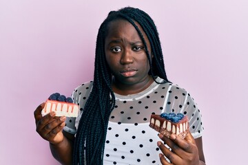 Poster - Young black woman with braids holding cheesecakes skeptic and nervous, frowning upset because of problem. negative person.