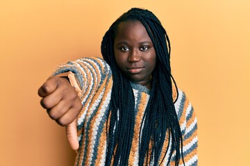 Wall Mural - Young black woman with braids wearing casual winter sweater looking unhappy and angry showing rejection and negative with thumbs down gesture. bad expression.