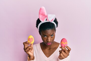 Canvas Print - Young african american girl wearing cute easter bunny ears holding painted eggs skeptic and nervous, frowning upset because of problem. negative person.