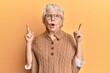 © Krakenimages.com - Senior grey-haired woman wearing casual clothes and glasses amazed and surprised looking up and pointing with fingers and raised arms.