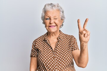 Wall Mural - Senior grey-haired woman wearing casual clothes smiling with happy face winking at the camera doing victory sign. number two.