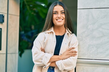 Wall Mural - Young hispanic girl with crossed arms smiling happy at the city.