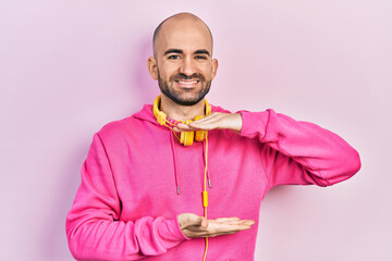 Canvas Print - Young bald man wearing gym clothes and using headphones gesturing with hands showing big and large size sign, measure symbol. smiling looking at the camera. measuring concept.