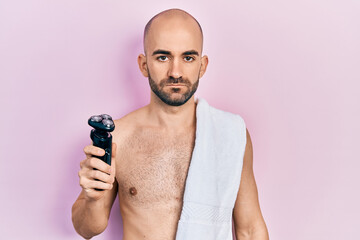 Canvas Print - Young bald man shirtless holding electric razor thinking attitude and sober expression looking self confident