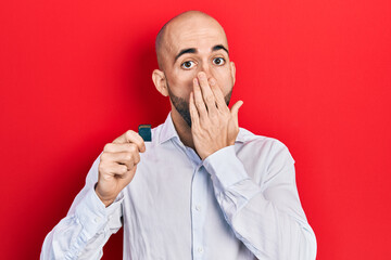 Wall Mural - Young bald man holding sdxc card covering mouth with hand, shocked and afraid for mistake. surprised expression