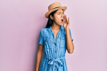 Poster - Young chinese woman wearing summer hat shouting and screaming loud to side with hand on mouth. communication concept.