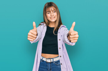 Teenager caucasian girl wearing casual clothes approving doing positive gesture with hand, thumbs up smiling and happy for success. winner gesture.